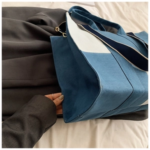 Detail of color-block denim tote bag showing blue stitching and wide fabric handle