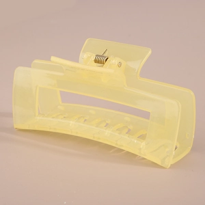 Detail view of a rectangular matte light yellow hair claw with a visible metal spring