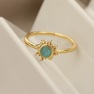 Golden sun-shaped open ring with round teal cat eye stone on white geometric stand