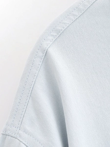 Macro detail of fine stitching and twill denim texture on a light blue casual shirt jacket