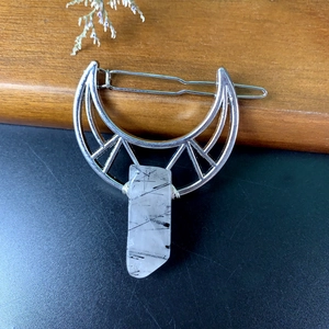 Detailed close-up of a silver crescent moon hair clip with a clear quartz crystal pendant