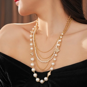 Detail of layered gold necklace with imitation pearls and sparkling rhinestone clovers