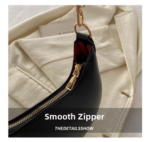 Detail of smooth black leather bag with golden zipper and contrasting red inner lining