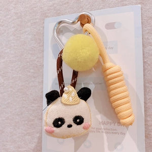 Detail of panda plush keychain with embroidered face, yellow pompom and braided rope strap