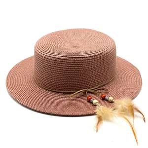 Detail of pink woven straw boater hat with bohemian feathers and beaded cord decoration