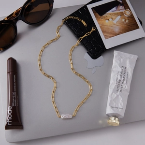 Gouden paperclip ketting met barokke parelhanger op een zilverkleurige laptop
