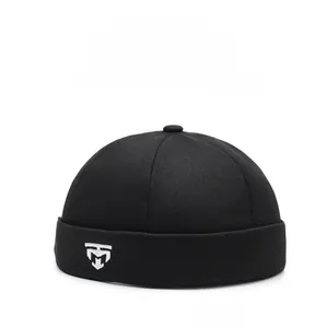 Detail of black cotton docker cap featuring white shield embroidery and twill texture