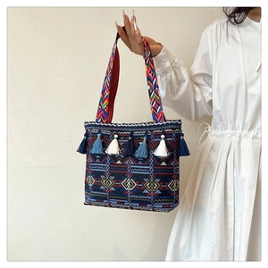 Ethnic woven tote bag with geometric patterns and colorful tassel charms shown on model