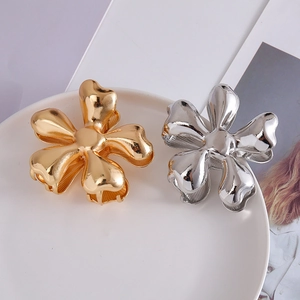 Glossy gold and silver flower hair claws in a minimalist metal design on a white ceramic plate