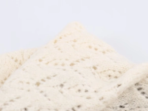 Macro shot of cream knit fabric with intricate hollow lace weaving details