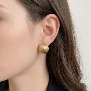 Elegant gold semi-spherical stud earrings with textured matte finish on female model