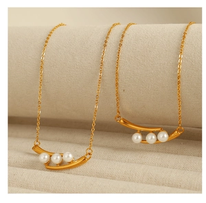 Détail du collier de perles montrant une barre dorée et trois perles rondes blanches ici