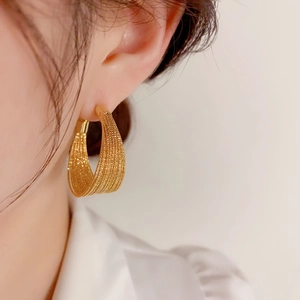 Close-up of golden mesh woven C-shape hoop earrings on a model showing fine texture
