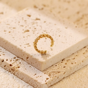 Close-up of gold ear cuff with shimmering diamonds on textured beige stone surface
