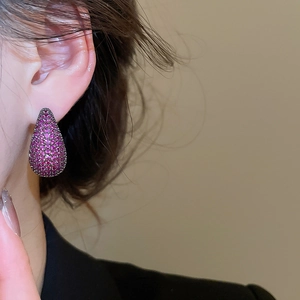 Close-up of elegant teardrop earrings featuring fuchsia zircons and dark metal plating