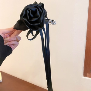 Détail de la pince à cheveux rose en tissu noir avec rubans et strass étincelants