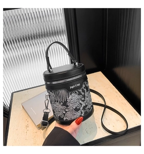 Detail of black cylinder bucket bag featuring white embroidery and silver zipper closure