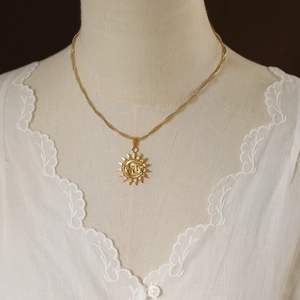 Golden sun pendant necklace on a mannequin wearing elegant white lace clothing