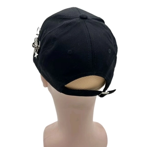 Détail de la casquette noire avec anneaux métalliques, trombones et pendentifs en étoile