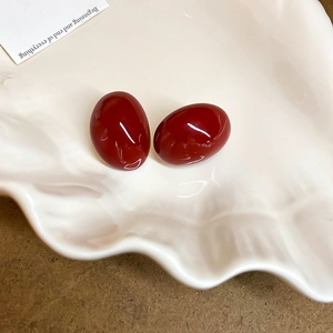 Close-up of minimalist dark red oval stud earrings presented on a decorative shell tray