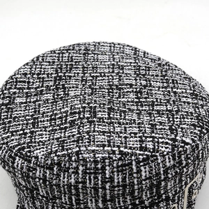 Close-up of black and white tweed newsboy hat featuring metallic button and gold silk thread