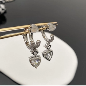 Détail de boucles d'oreilles cœur en argent avec cristaux étincelants tenues par une pince