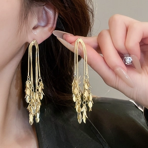 Detail of long golden tassel earrings with leaf charms shown on a female model