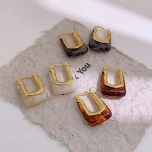 Detail view of U-shaped gold-plated resin earrings with marble and amber textures