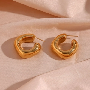 Detail shot of thick gold C-shaped hoop earrings on elegant light pink satin fabric