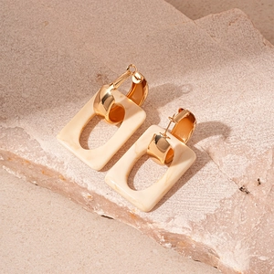 Detailed view of geometric cream resin earrings with polished gold metal hardware