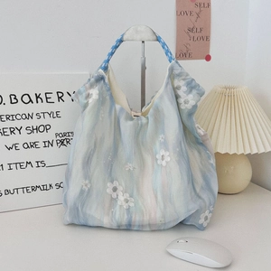 Detail of white floral embroidery and woven rope handle on a blue tulle handbag