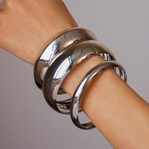 Detailed view of a 3-piece set of polished silver metal bangles worn on a model's wrist
