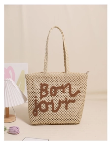 Detail of embroidered Bonjour letters on beige woven straw tote bag with zipper