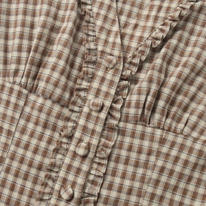 Detailed close-up of brown plaid fabric with ruffles and covered buttons on V-neckline