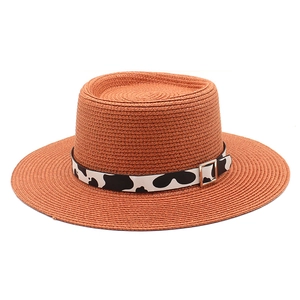 Detail of orange straw sun hat with cow print ribbon and golden square buckle