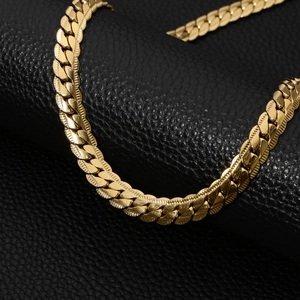 Macro detail of golden stainless steel flat Cuban link chain on black leather background