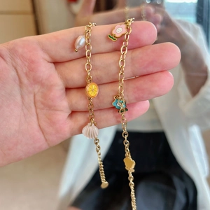 Golden bracelet with pearl, shell, lemon, and sunflower charms held by hand