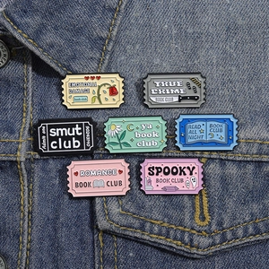 Collection of colorful enamel book club pins displayed on a blue denim jacket pocket
