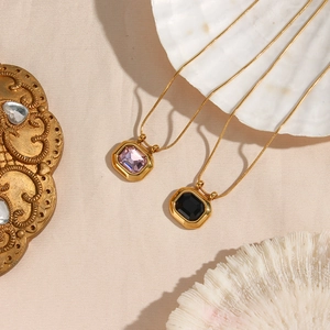 Detail of 18K gold necklaces with square pink and black zircon pendants on beige surface
