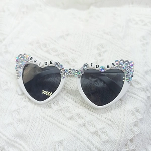 Close-up of heart-shaped bride sunglasses with iridescent rhinestones on white lace