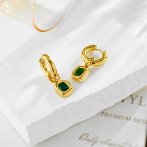 Golden hoop earrings with square emerald pendant on a natural stone background