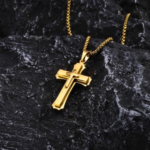 Macro shot of double-layered gold stainless steel cross pendant on black rock surface