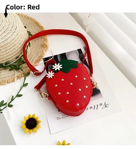 Detail of red strawberry crossbody bag with leaf accent and gold studs on a white table