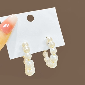 Close-up of elegant C-shaped pearl earrings on a white display card held by hand