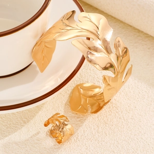 Detail of gold leaf cuff bracelet and ring set hanging on a white coffee cup