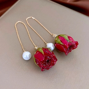 Detail of red rose drop earrings with pearls and gold chains on a silk fabric background