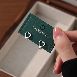 Minimalist S925 sterling silver hollow heart hoop earrings on dark green display card
