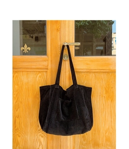 Detail of black corduroy tote bag with large front pocket hanging on wooden door
