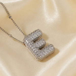 Collier lettre E argenté avec oxydes de zirconium sur fond luxueux en soie satinée