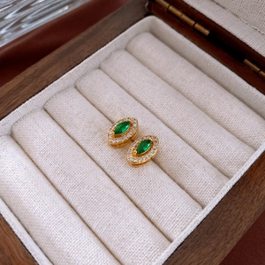 Detailed macro shot of vintage gold earrings with green stones in a luxury wooden box